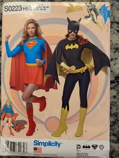 two people in costumes standing next to each other on a carpeted floor, one wearing a batman costume and the other as a supergirl