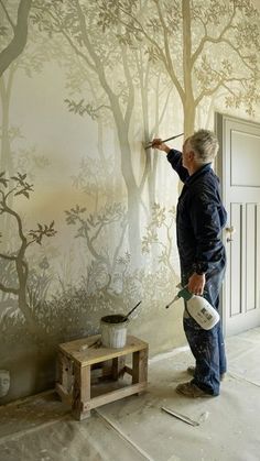 a man painting a wall with trees on it