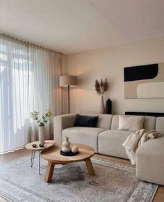 a living room filled with furniture and a large window covered in white drapes next to a wooden coffee table