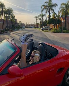 a woman sitting in the driver's seat of a red sports car with her feet up