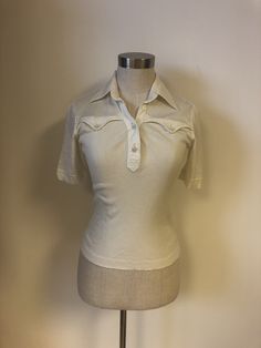 Awesome vintage tee from the 70s by Enea Gabrielli.  Off white with two pretend chest pockets. Semi sheer soft fabric at top part and sleeves and a ribbed fabric from chest pockets down at front and at back.  Great condition! But top button is missing and a little thread has come off the seam on the sleeve edge trim. 100% cotton Marked size 42 but estimated size S/M Please check measurements. Measurements taken laying flat; (Stretchy fabric) Shoulders 14,5" Bust 16,5" Waist 13 3/4" Length "21" Sleeves 8" Feel free to contact me with any questions! Retro Collared Tops With Pockets, Fitted White Tops With Pockets, White Fitted Tops With Pockets, White Fitted Retro Top, Fitted Short Sleeve Tops With Pockets, Retro Fitted White Top, Retro Cotton Tops With Pockets, Vintage Tops With Pockets For Spring, Vintage Spring Tops With Pockets