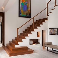 there is a painting on the wall next to some stairs in this living room with white walls and wood flooring