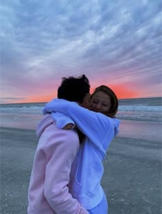 two people hugging each other on the beach at sunset, with clouds in the background