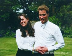 a man and woman standing next to each other in front of green grass with trees behind them