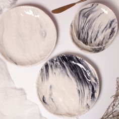 three plates with black and white designs on them next to some dried flowers, one has a spoon in it