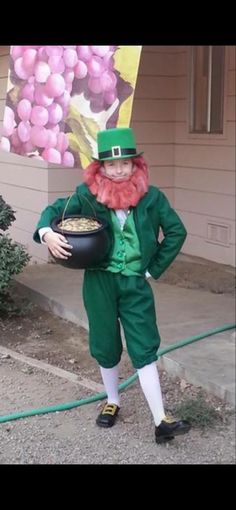 a man dressed as a lepreite holding a pot of gold in front of a house