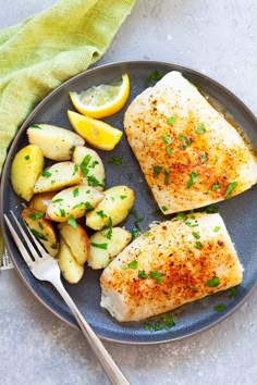 two fish fillets on a plate with potatoes and lemons next to a fork