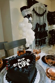 a black cake sitting on top of a table next to wine glasses and white balloons