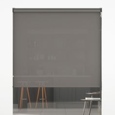 an empty table and chair in front of a large window with grey roller shades on it