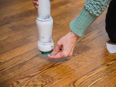 a person holding onto a white pipe on the floor with wood floors in the background