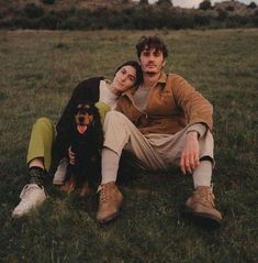 a man and woman sitting in the grass with their dog