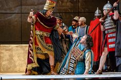 a group of people dressed in roman costumes standing on stage with one person pointing at the other