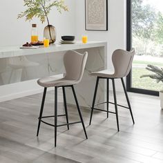 two stools sitting in front of a counter with drinks on it and an orange vase