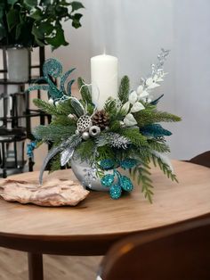 a wooden table topped with a vase filled with flowers and greenery next to a candle