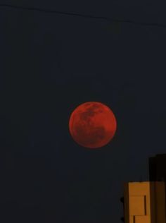 the red moon is visible in the dark sky above an apartment building on a city street