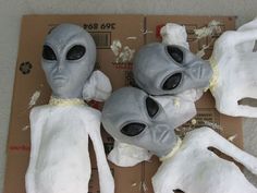 three plastic alien heads sitting on top of a piece of cardboard with torn up pieces of paper