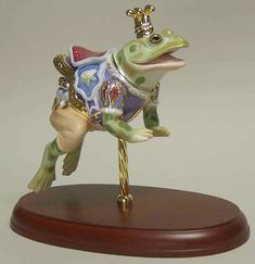 a figurine of a frog on top of a wooden base with an ornament hanging from it's back