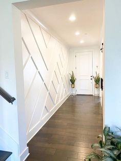 an empty hallway with white walls and wooden flooring, plants on either side of the door