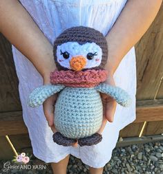 a crocheted penguin with a scarf around its neck is held by a woman