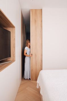 a woman in a white dress is looking at her phone while standing next to the bed