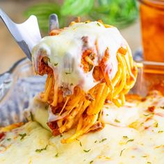 a fork full of spaghetti being lifted from the casserole dish with meat and cheese