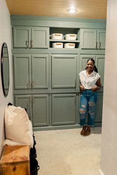 a woman standing in the corner of a room with lots of cupboards and drawers