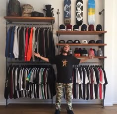 a man standing in front of a rack full of hats and shirts with his arms out