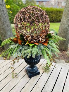 a vase filled with greenery on top of a wooden table next to some trees