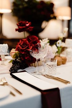 the table is set with white and red flowers, silverware, and wine glasses