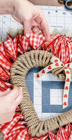 someone making a heart shaped wreath with twine and burlocks on the table