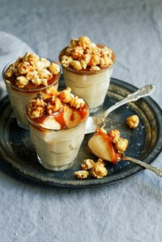 three desserts with caramel and walnut toppings on a black plate next to a spoon