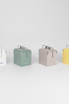 four different colored lunch boxes sitting side by side on a white surface, with one empty and the other closed