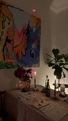 a dining room table with flowers and candles on it in front of a large painting