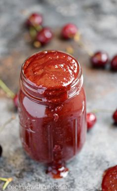 a jar filled with red liquid sitting on top of a table next to cherries