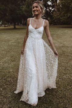 a woman standing in the grass wearing a white dress with stars on it and her hands behind her back