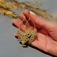 a person is holding some kind of gold earring in their hand and it looks like an intricate design