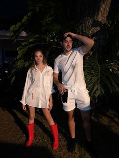 a man and woman dressed in white standing next to each other under a tree at night