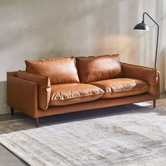 a brown leather couch sitting on top of a rug in a living room next to a lamp