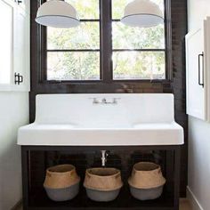 a white sink sitting under two windows next to a window covered in light fixturees