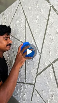 a man holding a blue object in his right hand and looking at the wall behind him