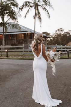 a woman in a white dress holding a bouquet and looking at the back of her dress