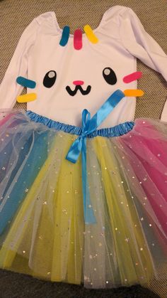 a white shirt with rainbow colored tulle skirt and cat face on the front, sitting on top of a carpet