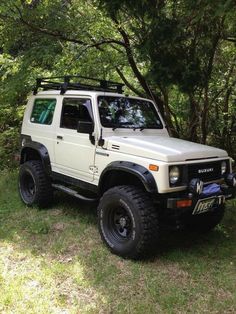 an off - road vehicle is parked in the grass near some trees and bushes on a sunny day