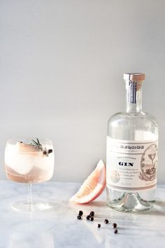 a bottle of gin next to a glass filled with ice and garnishes