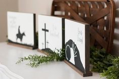 three wooden signs with black and white designs are on a table next to greenery