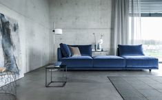 a living room with concrete walls and blue couches on the floor, along with large windows