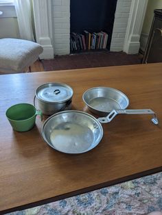 three metal pans sitting on top of a wooden table next to a green cup