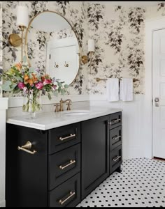 a black and white bathroom with flowers on the counter top, gold faucet