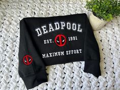 a deadpool sweatshirt laying on top of a crocheted blanket next to a potted plant