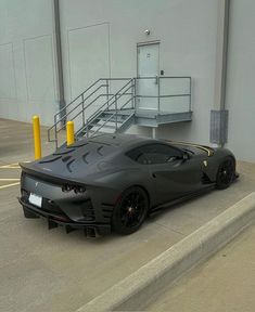 a black sports car parked in front of a parking garage with stairs leading up to it